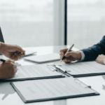Professional business meeting showing business purchase agreement being signed with documents and handshake